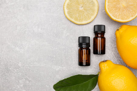 Bottles of essential oil with lemons and leaf on gray table, flat lay. Space for textの写真素材
