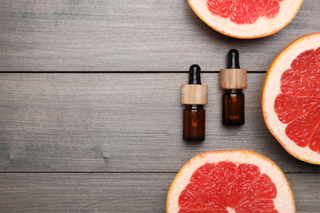 Bottles of citrus essential oil and grapefruit slices on wooden table, flat lay. Space for textの写真素材