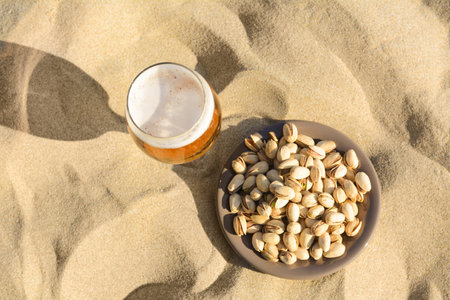 Glass of cold beer and pistachios on sandy beach, flat layの写真素材