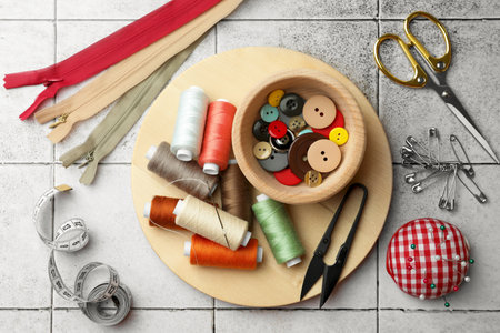 Flat lay composition with spools of threads and sewing tools on light tiles