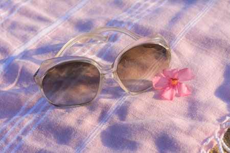 Beautiful sunglasses with tropical flower on pink blanket, closeupの写真素材