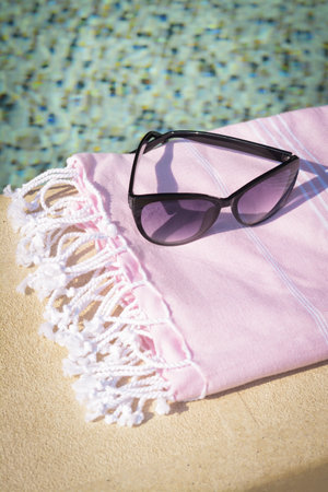 Stylish sunglasses and blanket near outdoor pool on sunny dayの写真素材
