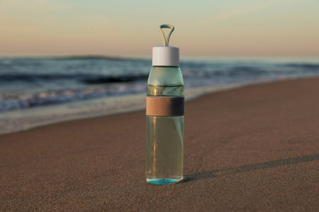 Glass bottle with water on wet sand near the sea at sunset
