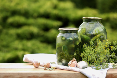 Jars of delicious pickled cucumbers and ingredients on wooden table against blurred background. Space for textの写真素材