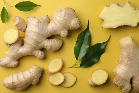 Fresh ginger with green leaves on pale light yellow background, flat lay