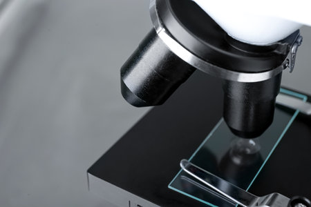 Modern medical microscope with glass slide on gray background, closeup. Space for text