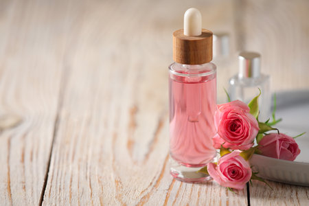 Bottle of essential rose oil and flowers on white wooden table, space for textの写真素材