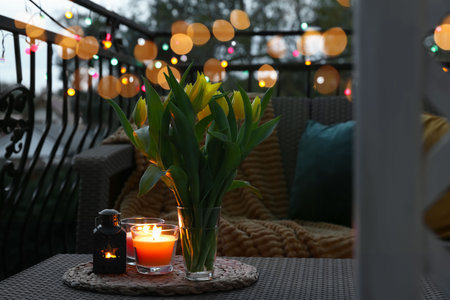 Soft pillows, blanket, burning candles and yellow tulips on rattan garden furniture in the eveningの写真素材