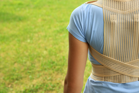 Closeup of woman with orthopedic corset on green grass outdoors, back view. Space for textの写真素材