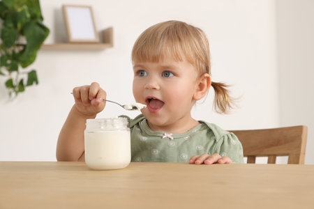 Cute little child eating tasty yogurt with spoon at wooden table indoorsの写真素材