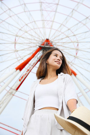 Beautiful young woman near Ferris wheel outdoors, low angle viewの写真素材