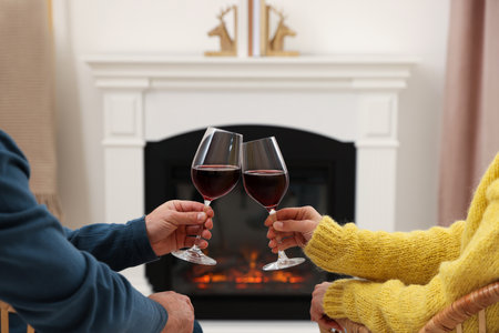 Lovely couple with glasses of wine spending time together near fireplace at home, closeupの写真素材