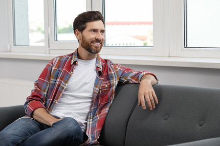 Smiling bearded man looking away on sofa indoorsの写真素材