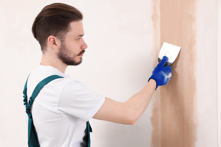 Worker in uniform plastering wall with putty knife indoorsの写真素材