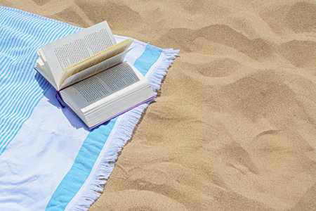 Beach towel with open book on sand, space for textの写真素材