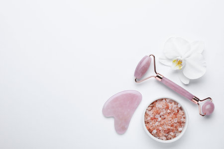 Gua sha stone, face roller, bath salt and orchid flower on white background, flat lay. Space for textの写真素材