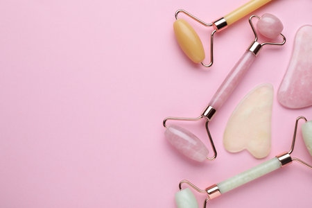 Different gua sha stones and face rollers on pink background, flat lay. Space for textの写真素材