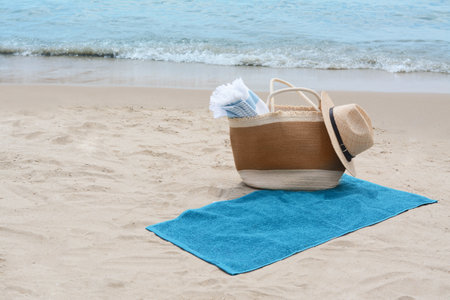 Bag with blanket, beach towel and straw hat on sandy seashore, space for textの写真素材