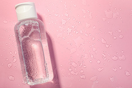 Wet bottle of micellar water on pink background, top view. Space for textの写真素材