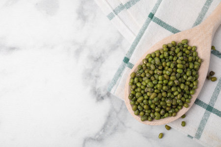 Wooden spoon with mung beans on white marble table, flat lay. Space for text