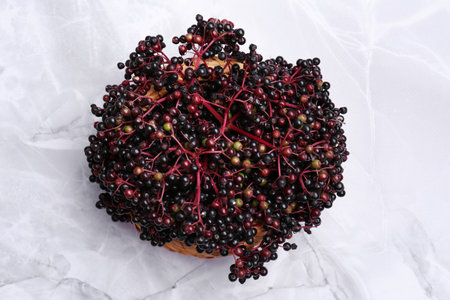 Tasty elderberries (Sambucus) on white marble table, top view