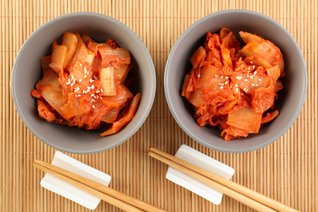 Bowls of spicy cabbage kimchi and chopsticks on bamboo mat, flat layの写真素材