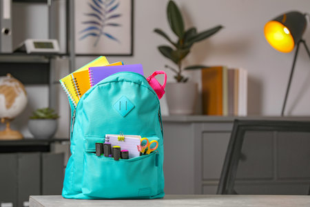 Turquoise backpack with different school stationery on table indoors, space for textの写真素材