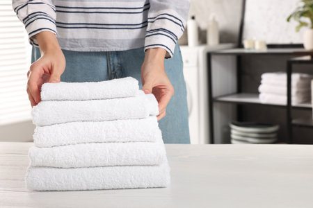 Woman stacking clean towels on white table in laundry room, closeup. Space for textの写真素材
