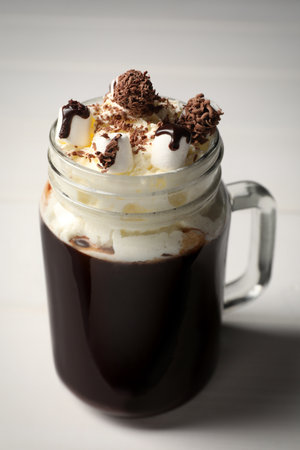 Mason jar of delicious hot chocolate with whipped cream on white wooden table, closeup