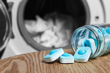 Jar with water softener tablets on wooden table near washing machine, space for text