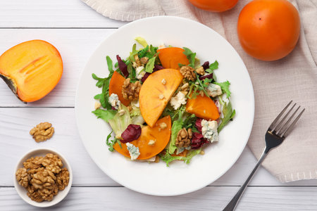Delicious persimmon salad and fork on white wooden table, flat layの写真素材