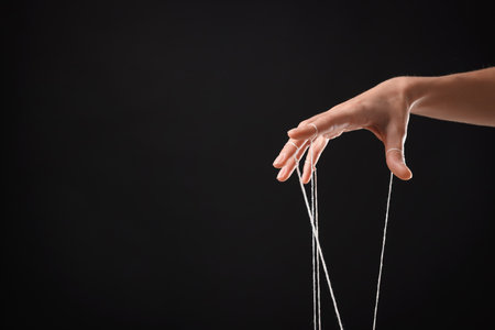 Woman pulling strings of puppet on black background, closeup. Space for textの写真素材