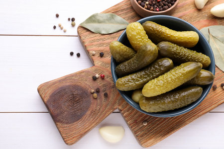 Tasty pickled cucumbers in bowl and ingredients on white wooden table, flat layの写真素材