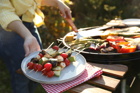 Woman cooking vegetables on barbecue grill outdoors, closeup