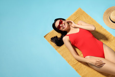 Young woman in stylish swimsuit on beach towel against light blue background. Space for textの写真素材