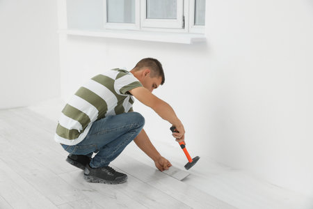 Professional worker using hammer during installation of new laminate flooring indoorsの写真素材