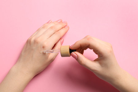 Woman dripping serum from pipette on her hand against pink background, closeupの写真素材