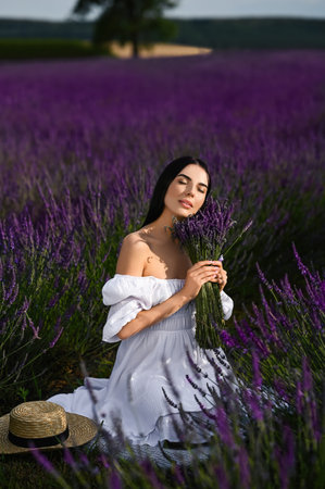 Beautiful young woman with bouquet sitting in lavender fieldの写真素材