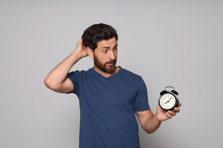 Emotional bearded man with alarm clock on light gray background. Being late concept