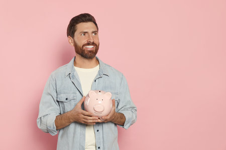 Happy man with ceramic piggy bank on pale pink background, space for textの写真素材