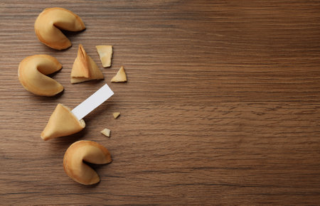 Tasty fortune cookies and paper with prediction on wooden table, flat lay. Space for textの写真素材