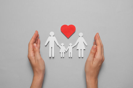Woman protecting paper family cutout on gray background, top view. insurance conceptの写真素材