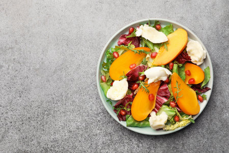 Delicious persimmon salad with cheese and pomegranate on gray table, top view. Space for textの写真素材