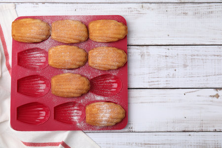 Delicious madeleine cookies in baking mold on white wooden table, top view. Space for textの写真素材