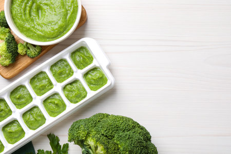 Broccoli puree in ice cube tray ready for freezing and ingredients on white wooden table, flat lay. Space for textの写真素材