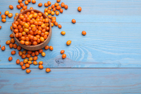 Bowl with fresh ripe sea buckthorn berries on light blue wooden table, above view. Space for textの写真素材