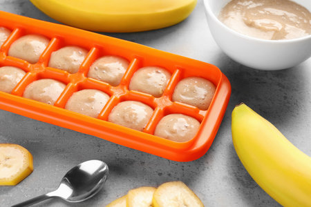 Banana puree in ice cube tray with fresh banana fruits on gray table. Ready for freezingの写真素材