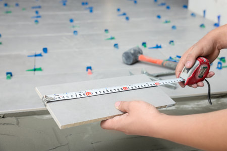 Worker measuring tile near adhesive mix on floor, closeupの写真素材