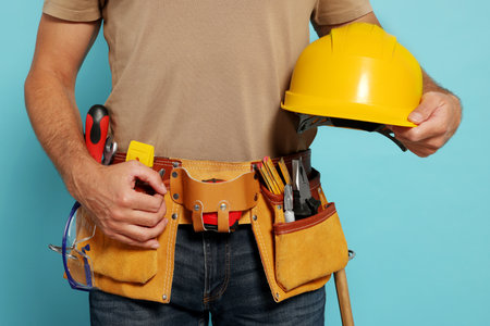 Professional builder with hard hat and tool belt on light blue background, closeupの写真素材