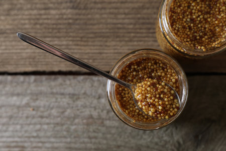 Jars and spoon of whole grain mustard on wooden table, flat lay. Space for textの写真素材